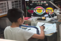 一小学生在闹市水果摊写作业 专注力引网友热议